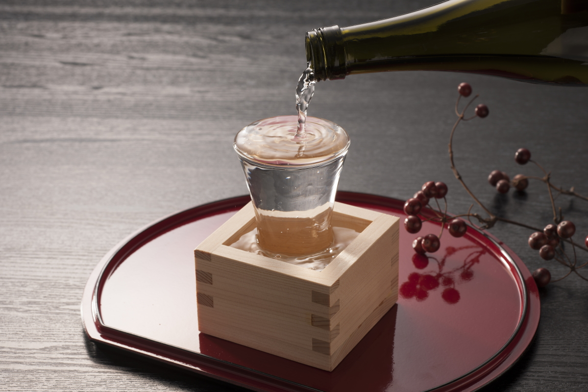 sake being poured into a glass in a wooden masu